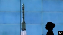 在北京，一名戴口罩的女子從電視屏幕前走過，電視屏幕上播放著搭載神舟十二號載人飛船的長征二號F遙十二運載火箭從酒泉衛星發射中心升空的景象。（2021年6月17日）