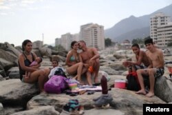 FILE - Leonel Martinez, who works as soldier, kisses his girlfriend as they spend a day at Coral beach in La Guaira near Caracas, Venezuela, March 23, 2019. "It's a way to think about something besides what is happening in the country," said Martinez. "It's not something you can do every day, because of the situation in the country."