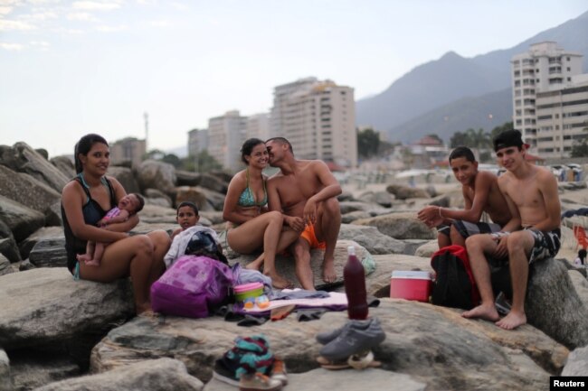 FILE - Leonel Martinez, who works as soldier, kisses his girlfriend as they spend a day at Coral beach in La Guaira near Caracas, Venezuela, March 23, 2019. "It's a way to think about something besides what is happening in the country," said Martinez. "It's not something you can do every day, because of the situation in the country."