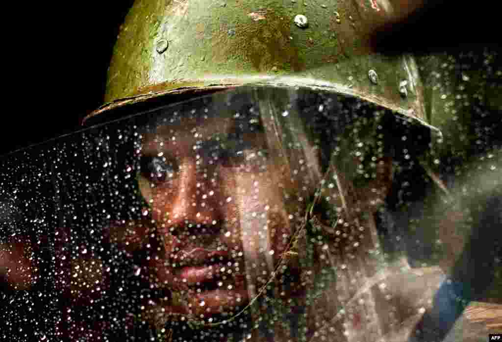 August 11: An police officer in New Dehli looks from behind his rain covered shield during a monsoon rain shower as he and others stand guard at a protest by the main opposition Bharatiya Janata Party. (AP Photo/Kevin Frayer)
