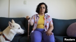 FILE - Leticia de Souza Soares, who suffers from pain and health problems caused by long COVID-19, holds a cane while sitting at home, in Salvador, Brazil, Dec. 8, 2023.