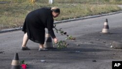 A woman puts flower on the ground in the spot where shell landed killing several people, in Sartana, on the outskirts of the town of Mariupol, eastern Ukraine, Oct. 15, 2014.