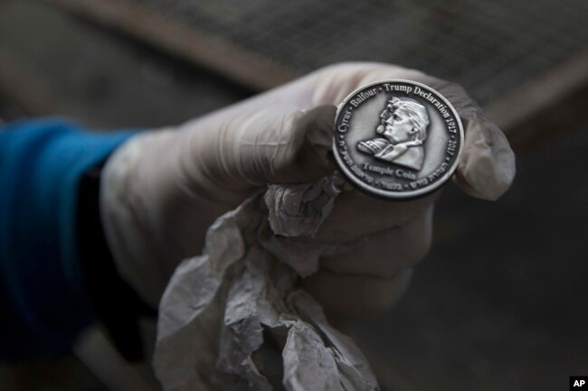 A worker holds a coin bearing the images of President Donald Trump and King Cyrus, to honor Trump's recognition of Jerusalem as Israel's capital, at a private minting facility, in Tel Aviv, Israel, Feb. 28, 2018.