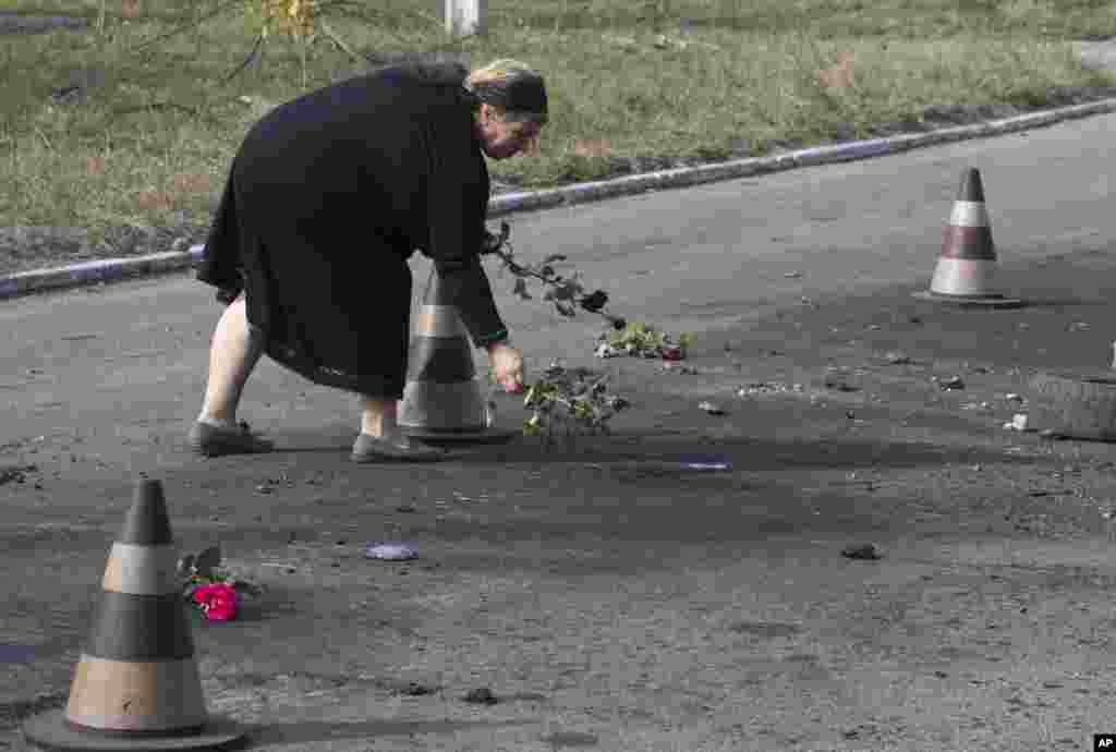 A woman puts flower on the ground in the spot where shell landed killing several people, on the outskirts of Mariupol, Ukraine, Oct. 15, 2014. 
