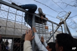 FILE - An Afghan refugee jumps the fence as he tries to enter Macedonia at the Greek-Macedonia borderline near the northern Greek village of Idomeni, Feb. 22, 2016.