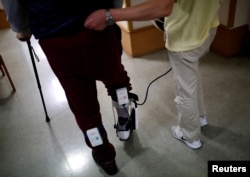 A caretaker (R), wearing walking rehabilitation equipment 'Tree', helps a resident with his walking training at Shin-tomi nursing home in Tokyo, Feb. 5, 2018.