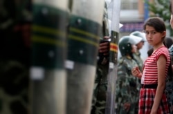 一名维吾尔族女孩儿站在中国武警手持的防暴盾前。（2009年7月9日）
