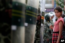 一名维吾尔族女孩儿站在中国武警手持的防暴盾前。（2009年7月9日）