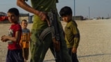 Boys observe an armed guard who patrols areas close to the market in al-Hol Camp, Northeast Syria on Oct. 12, 2024.