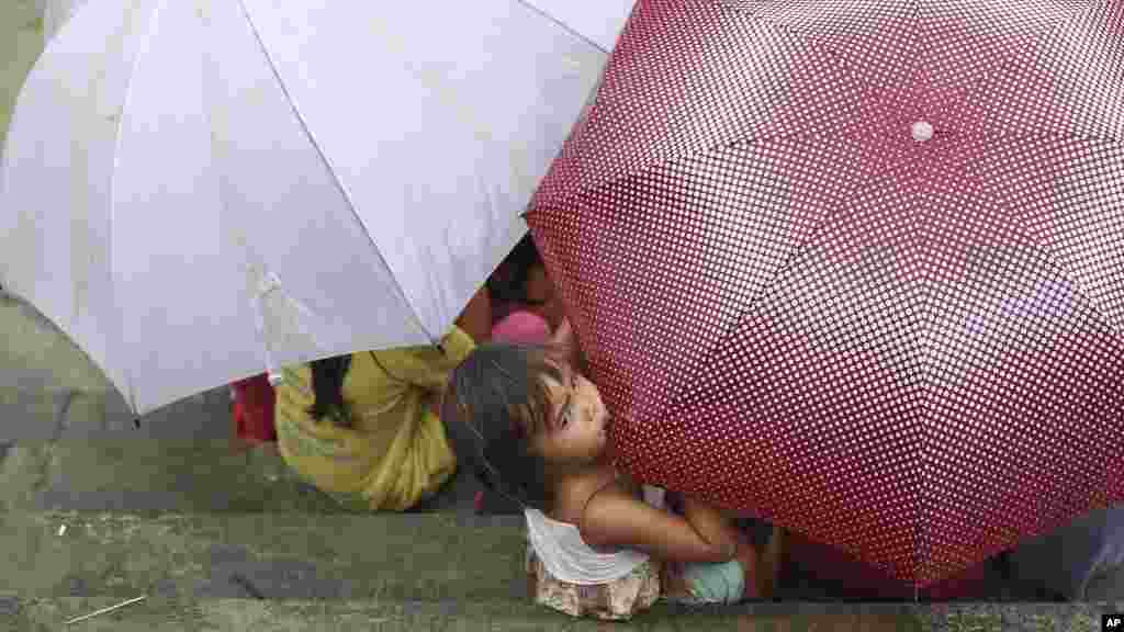 A Filipino girl bites an umbrella as her playmates take cover from rain in Makati, south of Manila, Philippines, Sept. 14, 2014.