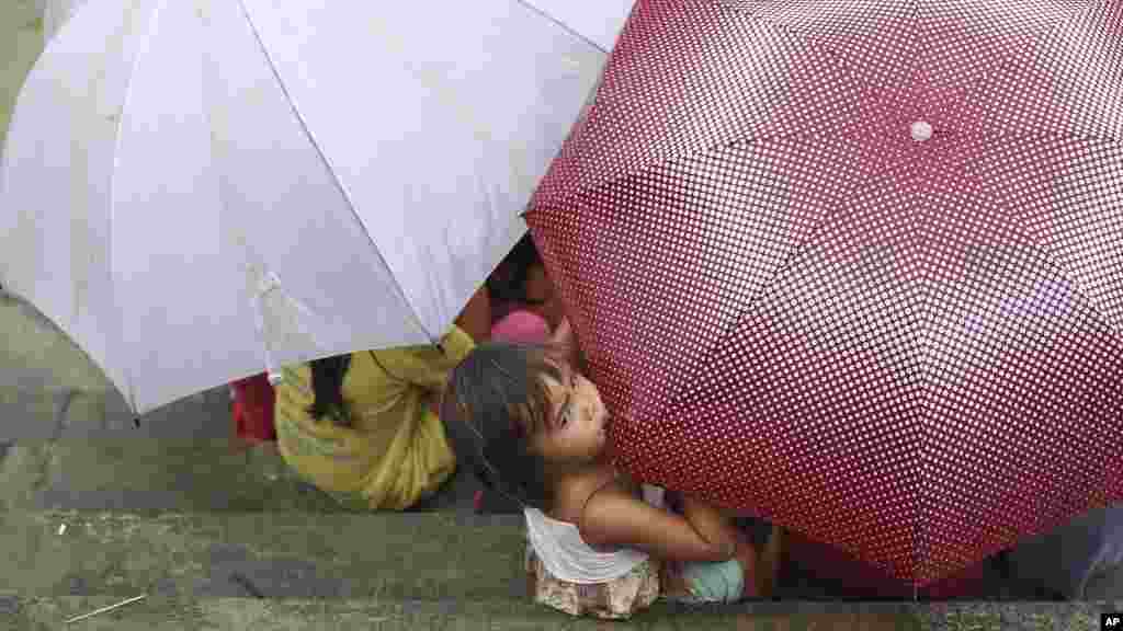 A Filipino girl bites an umbrella as her playmates take cover from rain in Makati, south of Manila, Philippines, Sept. 14, 2014. 