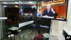 A man sits outside a restaurant while Algerian President Abdelmadjid Tebboune speaks on television, Feb.18, 2021, in Algiers.