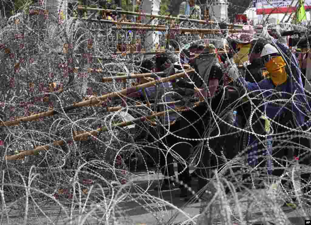 Anti-government protesters use a ladder as they try to remove barbed wire placed inside a gate at Government House in Bangkok, Dec. 12, 2013.