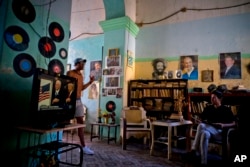 FILE - A man watches President Donald Trump's televised inauguration speech in Havana, Jan. 20, 2017. Behind him are photos, from left, of Cuban revolutionary Camilo Cienfuegos, late leader Fidel Castro and President Raul Castro.