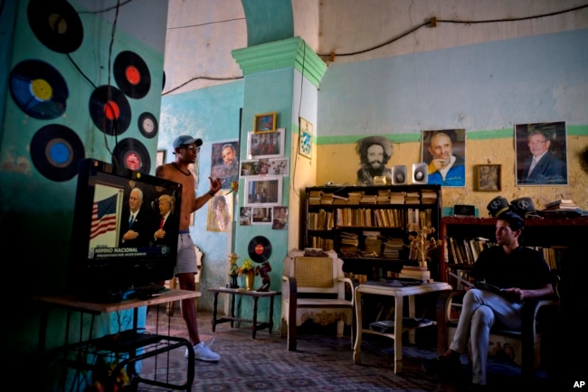 FILE - A man watches President Donald Trump's televised inauguration speech in Havana, Jan. 20, 2017. Behind him are photos, from left, of Cuban revolutionary Camilo Cienfuegos, late leader Fidel Castro and President Raul Castro.