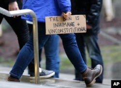 A person walks away from the federal courthouse in Seattle carrying a sign that reads "The Ban is Inhumane and Unconstitutional" following a hearing in federal court in Seattle, Feb. 3, 2017.