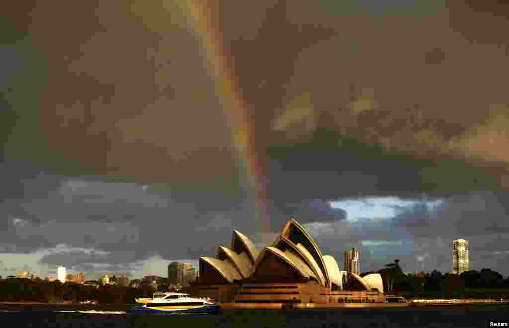 Sebuah kapal feri melewati Gedung Opera di kota Sydney, sementara pelangi terlihat di langit pada sore hari yang cerah saat musim dingin di Sydney, Australia.