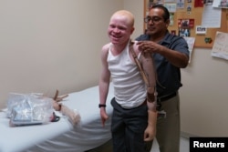 A worker helps Emmanuel Rutema, a Tanzanian with albinism who had his arm chopped off in a superstition-driven attack, put on a new prosthetic arm at the Shriners Hospital in Philadelphia, Pennsylvania, May 30, 2017.