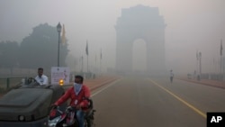 FILE - A man covers his face as he rides in front of the landmark India Gate, enveloped by smoke and smog, in New Delhi, India, Oct. 31, 2016. As Indians wake to smoke-filled skies from a weekend of festival fireworks for the Hindu holiday of Diwali, New Delhi's worst season for air pollution begins, with dire consequences. 