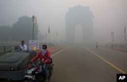FILE - A man covers his face as he rides in front of the landmark India Gate, enveloped by smoke and smog, in New Delhi, India, Oct. 31, 2016.