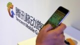 在北京舉行的全球移動互聯網會議上一名參觀者在騰訊展台前玩智能手機上的遊戲。 （2015年4月28日）