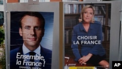 Election campaign posters for French centrist presidential candidate Emmanuel Macron and far-right candidate Marine Le Pen are posted in front of the polling station where Marine Le Pen will vote in Henin Beaumont, northern France, May 6, 2017. 