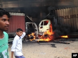 Indian youth walk past as two trucks that came from the neighboring Tamil Nadu state go up in flames during violence in Bangalore, Karnataka state, Sept. 12, 2016.