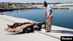 Um homem inspeciona os corpos de três africanos mortos, encontrados ao largo da costa de Tripoli, na Líbia. Set 15, 2014