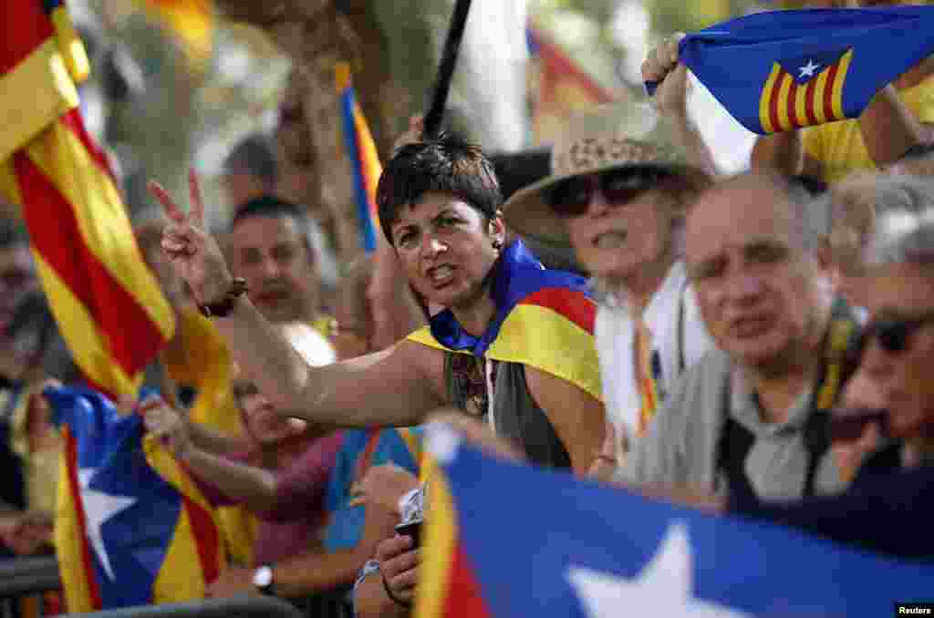 A Catalonian separatist supporter gestures with her hand as others wave Estelada flags, the flag flown by Catalonian separatists. They gathered in front of Catalonia's Parliament before the approval of a regional consultation law in Barcelona, Spain.