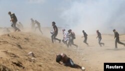 Des manifestants palestiniens tombent au milieu du gaz lacrymogène tiré par les forces israéliennes à la frontière entre Israël et Gaza, le 15 mai 2018