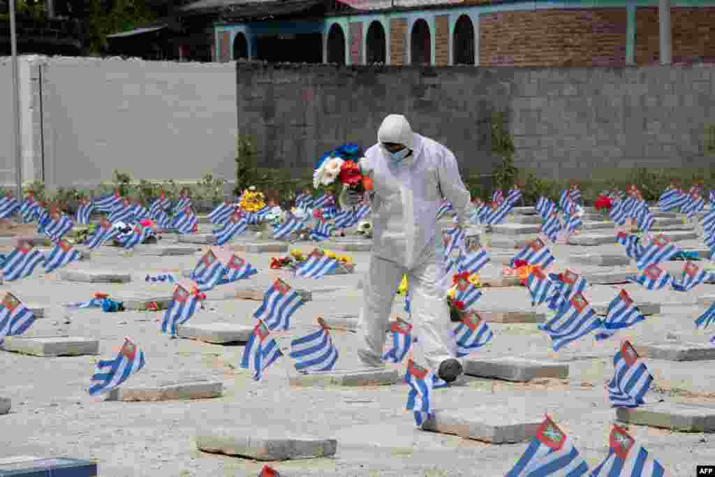 A municipal worker wearing a biosecurity suit carries flowers to be placed on the grave of a victim of COVID-19 at La Bermeja Cemetery during a Day of the Dead celebration, in San Salvador, El Salvador, Nov. 2, 2020.