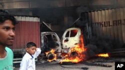 Indian youth walk past as two trucks that came from the neighboring Tamil Nadu state go up in flames during violence in Bangalore, Karnataka state, Sept. 12, 2016.