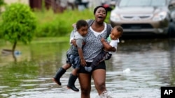 Terrian Jones reacts as she feels something moving in the floodwater at her feet as she carries Drew and Chance Furlough to their mother on Belfast Street in New Orleans, July 10, 2019.