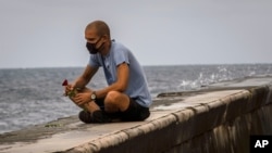 Un hombre que usa una mascarilla como precaución contra la propagación del nuevo coronavirus ofrece una rosa al mar en recuerdo de sus seres queridos durante el día de la madre.