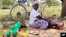 A woman sits on the ground beside a sleeping child, outside a small clinic in Gampela village on the outskirts of Burkina Faso's capital, Ouagadougou, Saturday Oct. 10, 2020. People sometimes wait up to four hours to get medical help. (AP Photo/Sam Mednick)
