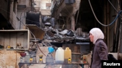 FILE - A woman walks past fuel for sale in Ein Terma, a district of eastern Ghouta, Syria, Feb. 26, 2019. 