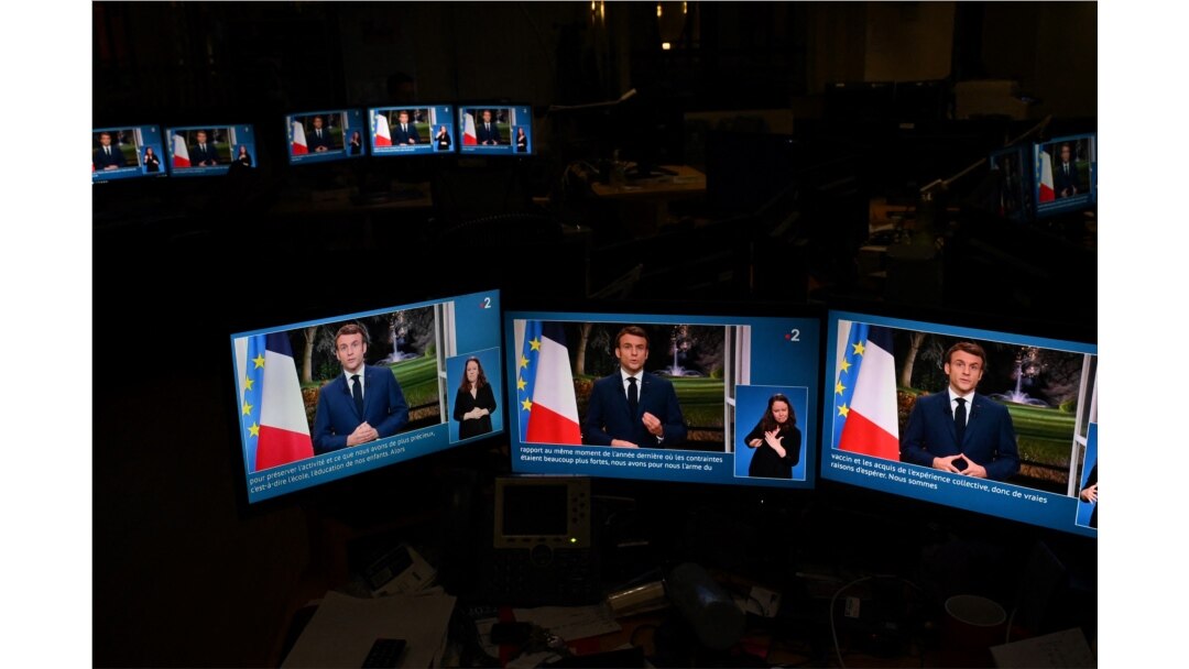 Images of French President Emmanuel Macron are seen on computer screens as he delivers his televised New Year's address to the nation from the Elysee Palace, in Paris on December 31, 2021.