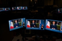 Images of French President Emmanuel Macron are seen on computer screens as he delivers his televised New Year's address to the nation from the Elysee Palace, in Paris on December 31, 2021.