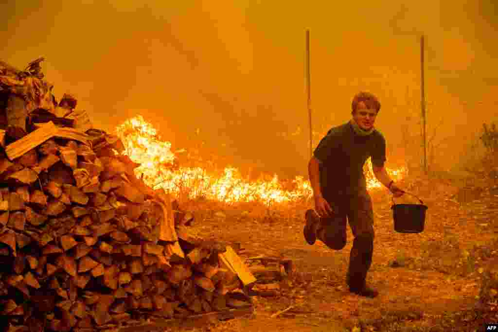 Alex Schenck carries a bucket of water while fighting to save his home as the Ranch Fire tears down New Long Valley Rd near Clearlake Oaks, California, Aug. 4, 2018.