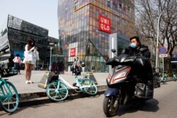 A man wearing a mask rides past a Uniqlo store in Beijing on March 25, 2021.