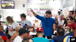 ARCHIVO - Franklin Virgüez, en el centro, lidera un cántico mientras él y otros venezolanos observan las noticias televisadas de su país en el restaurante venezolano El Arepazo Doral.