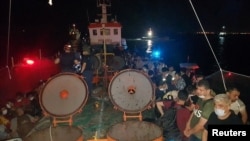 Anggota Komando Penjaga Pantai Turki berjaga-jaga di sebelah migran di geladak kapal kargo, saat penggerebekan di kota pelabuhan Aegean, Izmir, Turki, 7 Juli 2020.