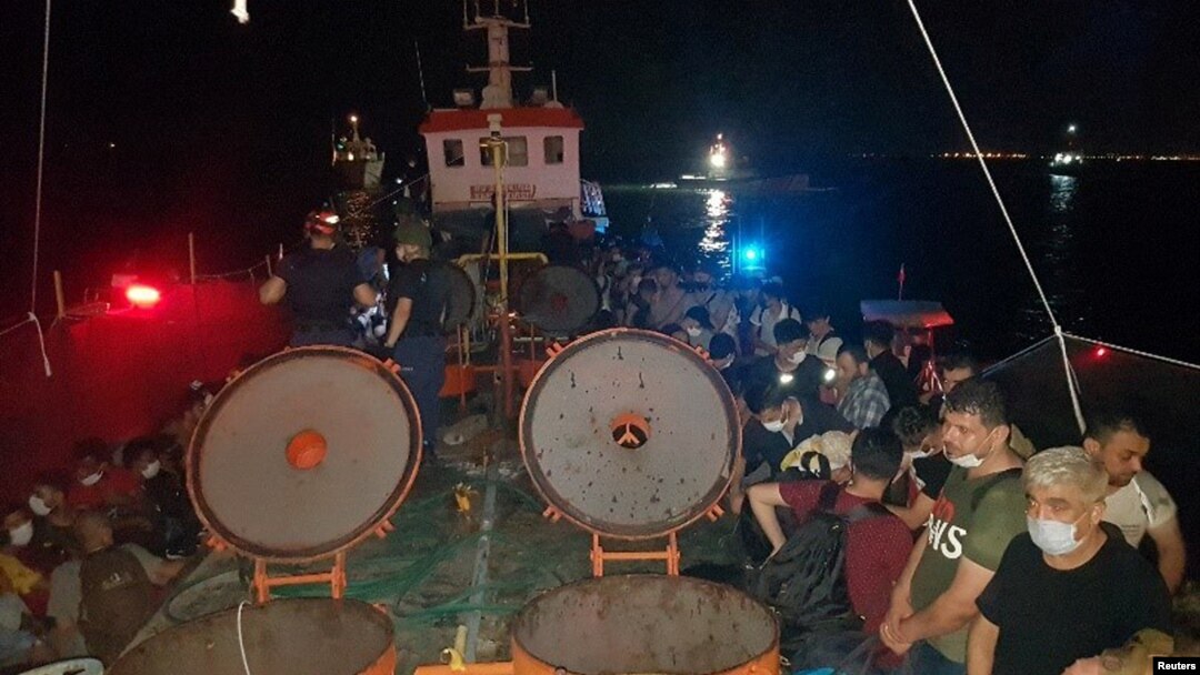 Anggota Komando Penjaga Pantai Turki berjaga-jaga di sebelah migran di geladak kapal kargo, saat penggerebekan di kota pelabuhan Aegean, Izmir, Turki, 7 Juli 2020.