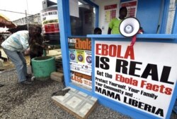 FILE - Liberians wash their hands next to an Ebola information and sanitation station, raising awareness about the virus in Monrovia, Sept. 30, 2014.