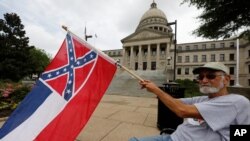 Larry Eubanks waves the current Mississippi state flag as he sits before the front of the Capitol, June 27, 2020, in Jackson, Miss. 