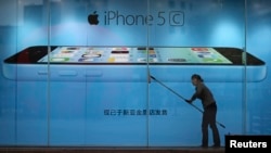 FILE - A worker cleans the windows in front of an iPhone 5C advertisement at an Apple store in Kunming, Yunnan province, China.