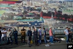 FILE - A group of men, mostly migrant laborers from Central Asian countries, stand next to a fence decorated with a picture of Moscow's Kremlin in Russia, July 5, 2016.