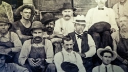 Foto de Jack Daniel (chapéu branco) sentado ao lado de George Green, filho de Nathan "Nearest" Green.