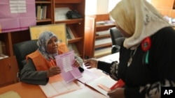 FILE - An election worker explains a ballot to a woman at a polling center during voting in the parliamentary elections in Tripoli, Libya, Wednesday, June 25, 2014. 