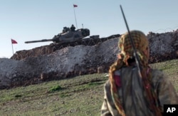 FILE - A Syrian Kurdish militia member of the YPG patrols near a Turkish army tank as Turks work to build a new Ottoman tomb in the background in Esme village in Syria's Aleppo province, Feb. 22, 2015.